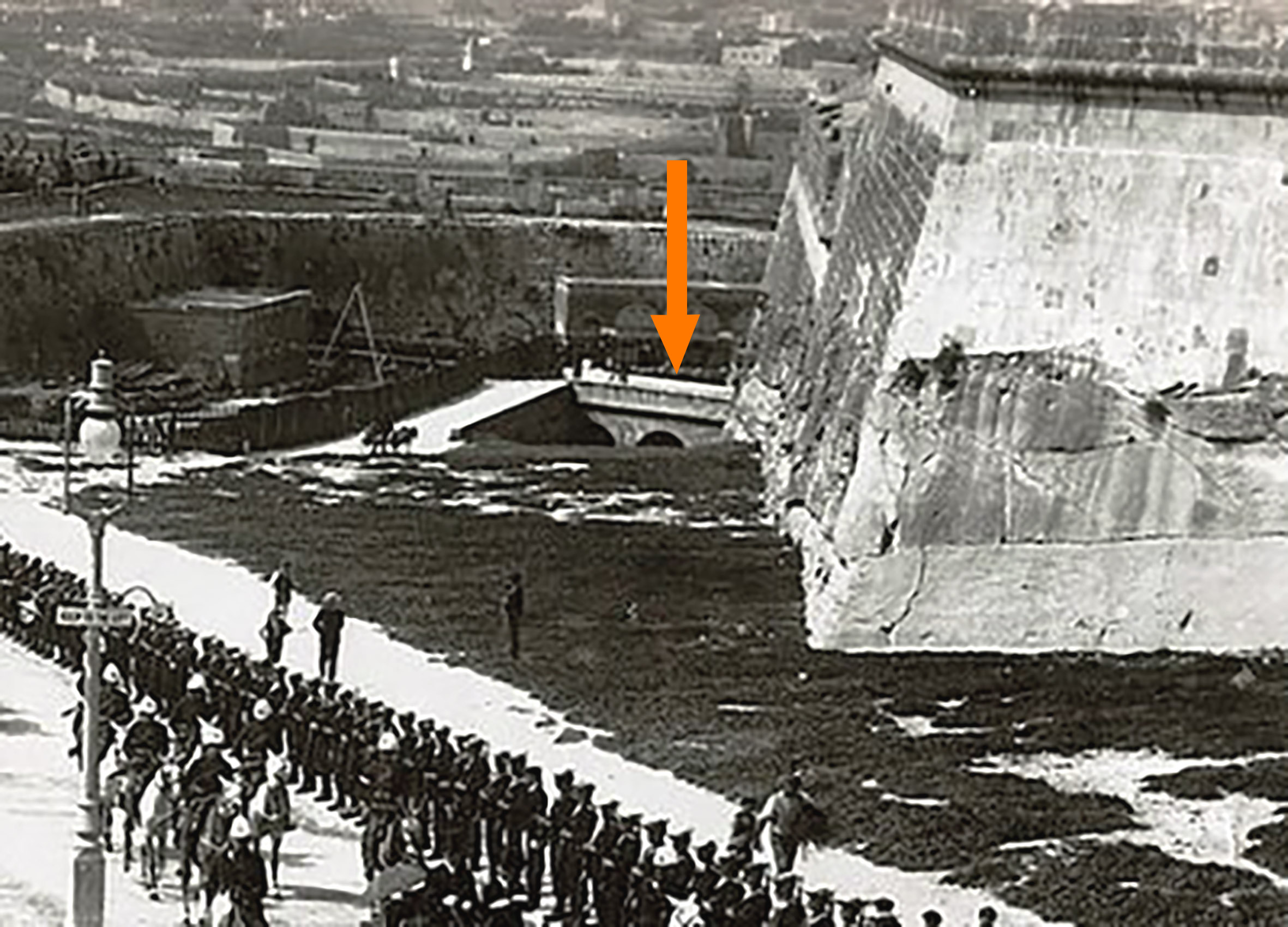 The replacement stone bridge in the Notre Dame ditch, visible across the drop ditch in which it sat entirely. This detail of a 1903 royal visit shows the bridge before the construction of guard hut No.1 in 1916,  roughly where the arrow ends.