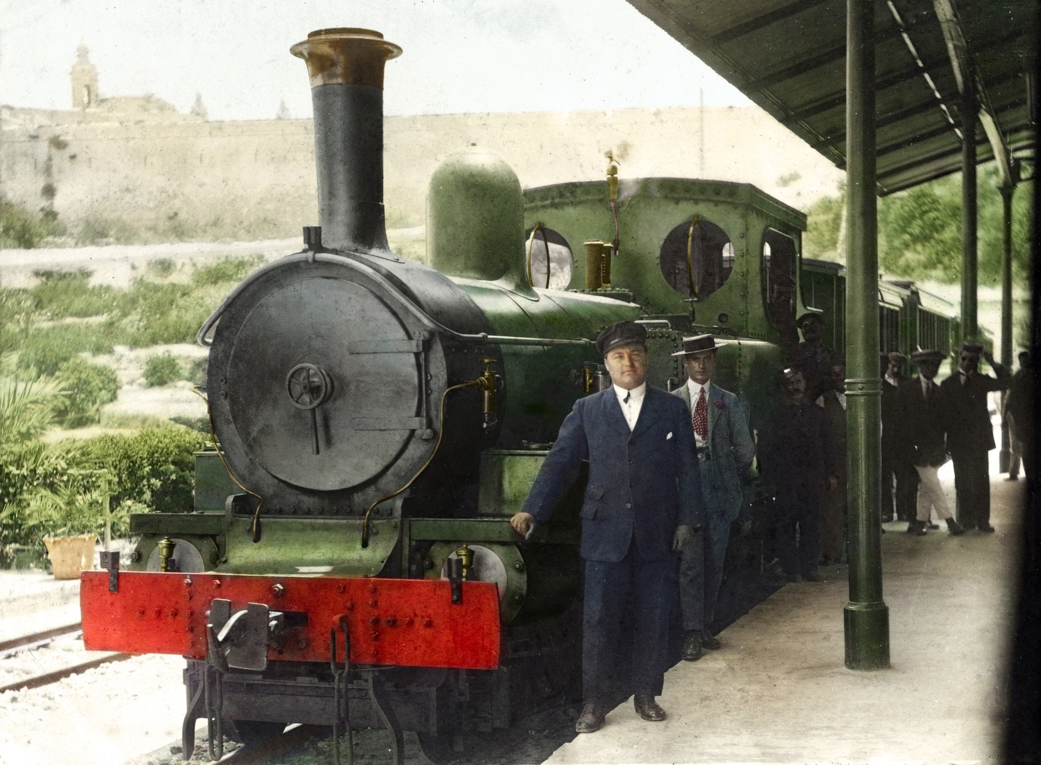 A Beyer Peacock locomotive is posed at the platform of Museum station with Mdina behind it.